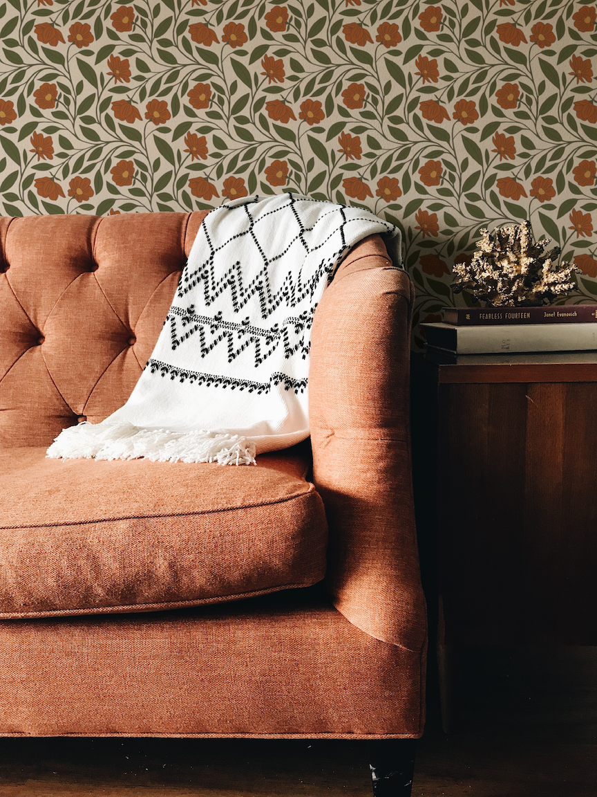 Brown sofa with a patterned throw blanket against a floral wallpapered wall.